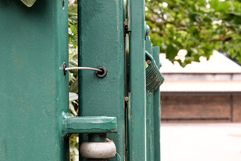 Gate restrainer safety cable installed in green metal gate