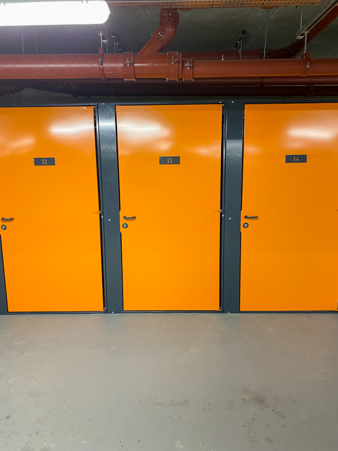 Drei Lagereinheiten mit Riegelschlössern. Die Türen sind gelb gestrichen und sitzen in grauen Rahmen