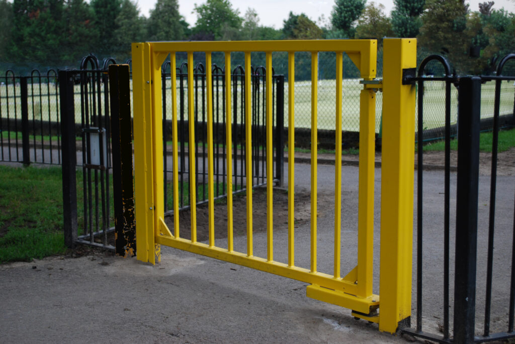 Mécanisme de fermeture de portail installé sur une porte piétonne jaune dans un centre de loisirs