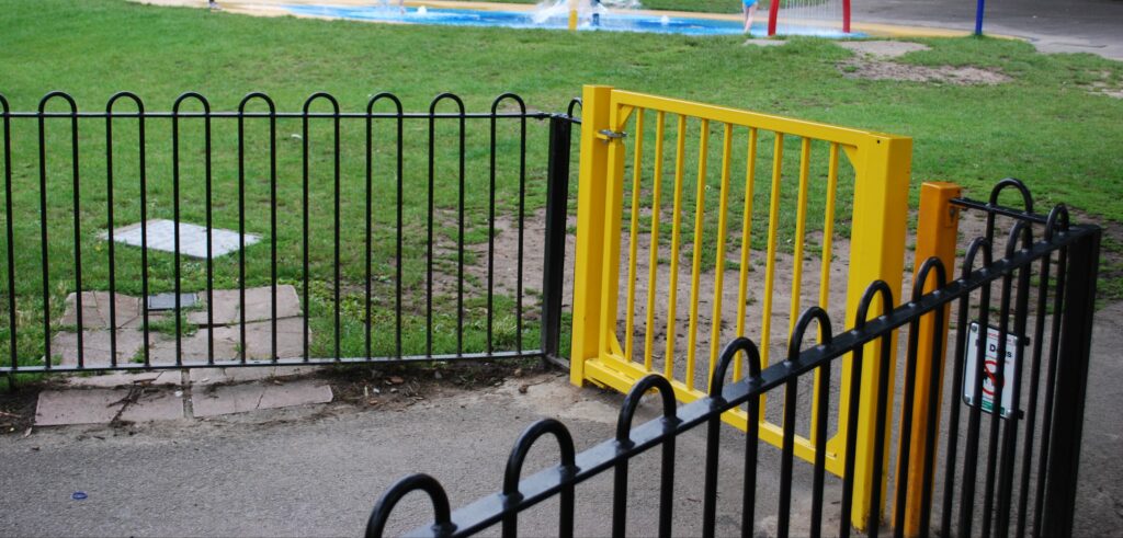 Porte à fermeture automatique installée sur la barrière jaune devant l'aire de jeux.