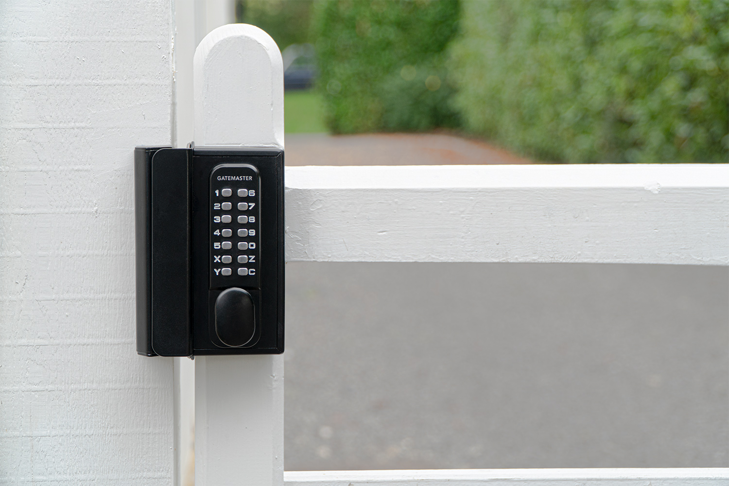Front of digital keypad lock with 14 digit keypad. Lock is fixed to white wooden garden gate