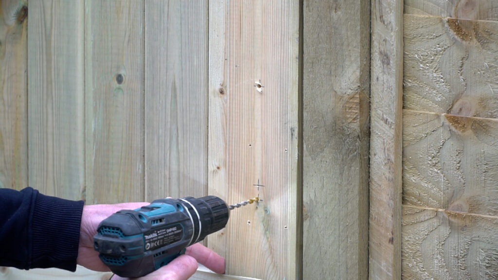 Person drilling two holes in wooden gate with power drill