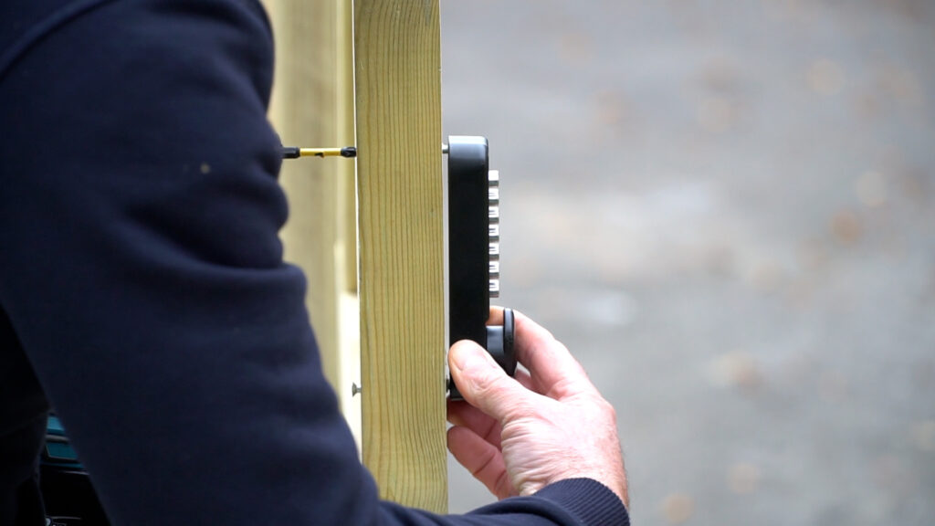 Personne qui installe un clavier numérique sur un portail en bois