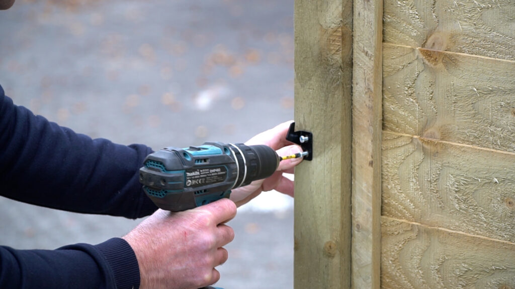 Personne munie d'une perceuse montant une gâche à verrou sur un poteau de portail en bois à l'aide d'une perceuse électrique