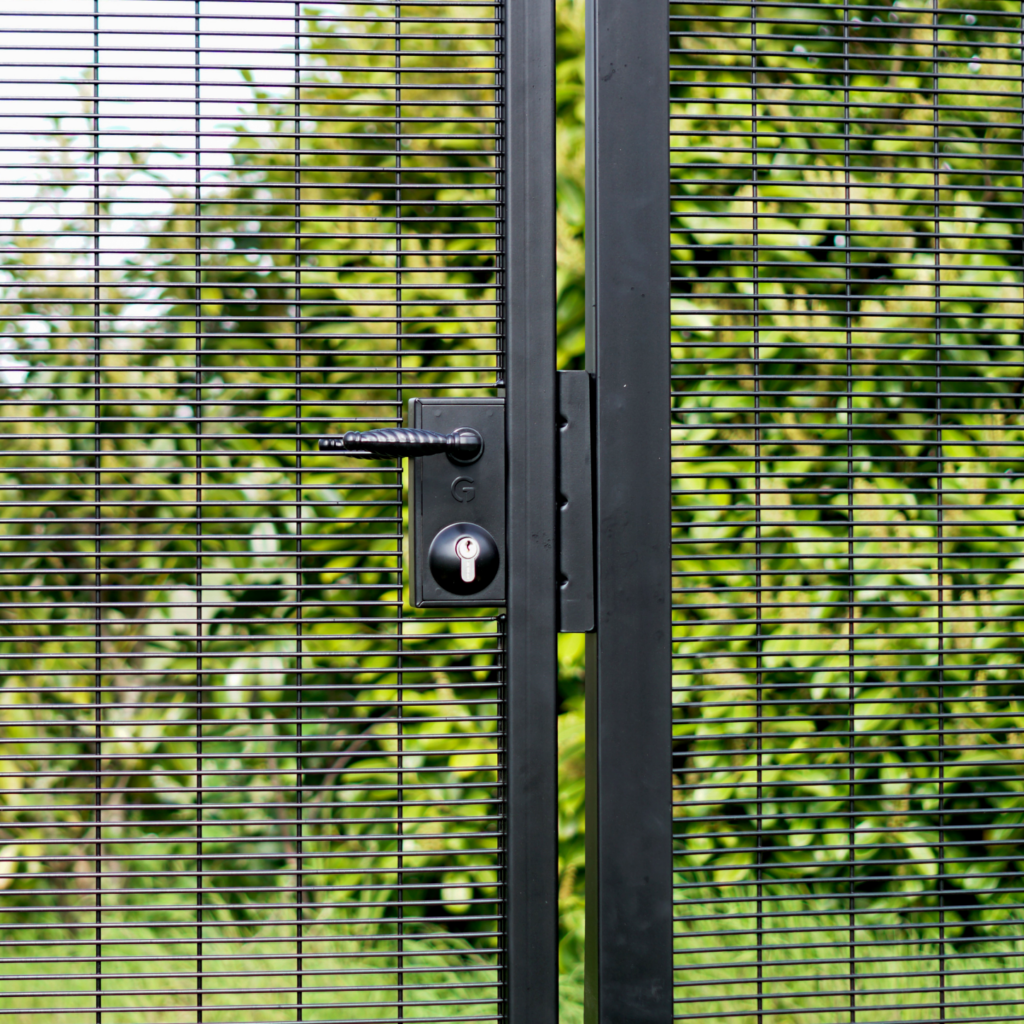 pêne dormant et demi-tour avec poignée d'ornement sur un portail en métal noir devant des arbustes verts