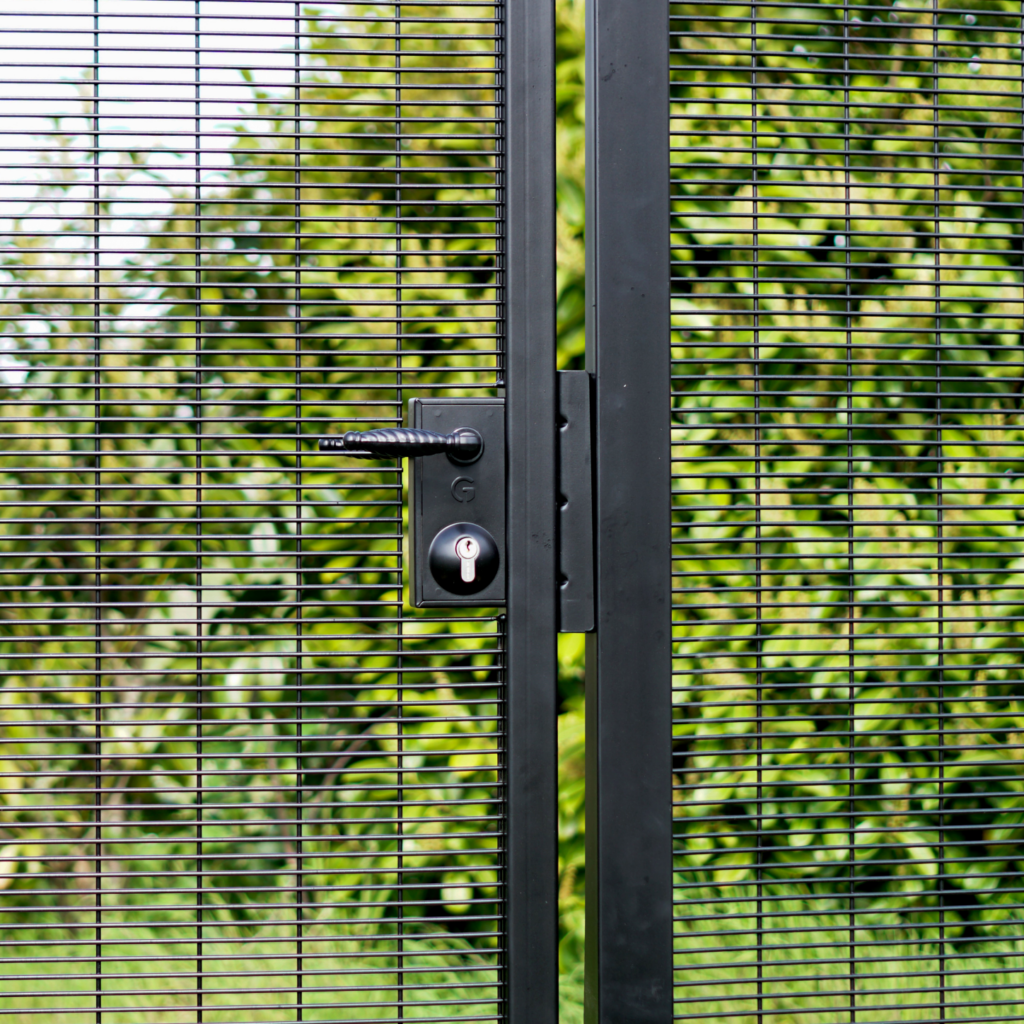 latching deadlock with ornate handle on black metal gate in front of green shrubbery