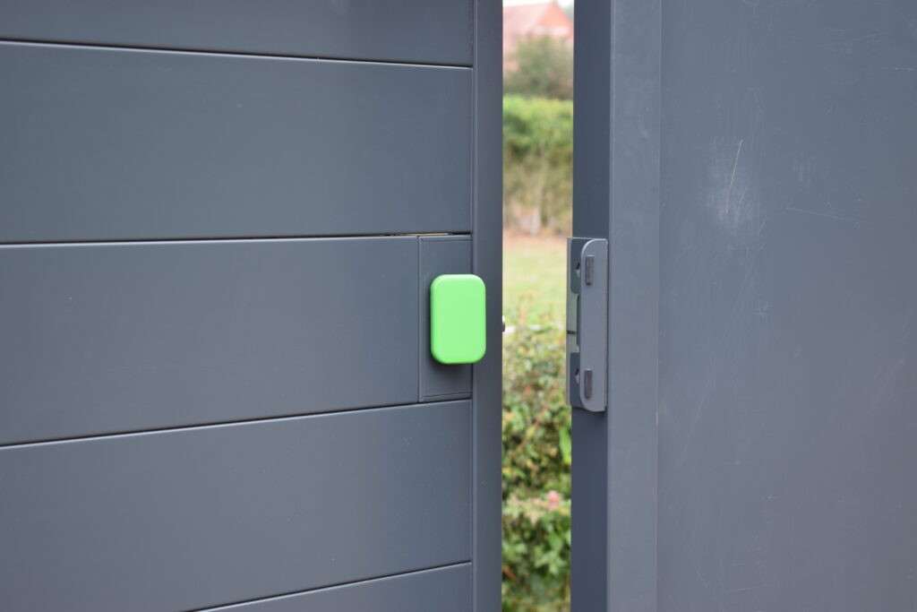 Gate lock with green push pad installed on grey metal infill gate