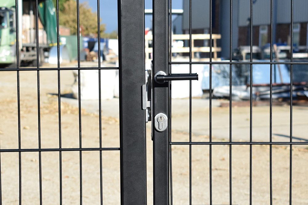 serrure à encastrer installée dans un cadre de portail devant un site industriel. 