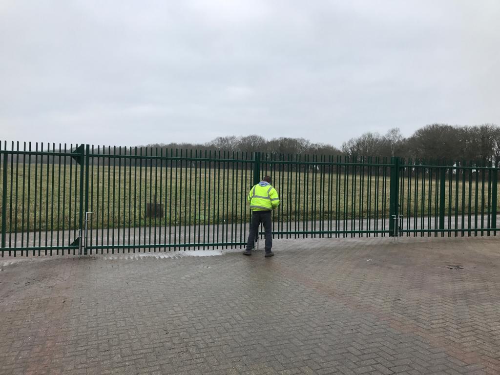 Man in high vis vest in front of large green metal bi fold gate with industrial hinges