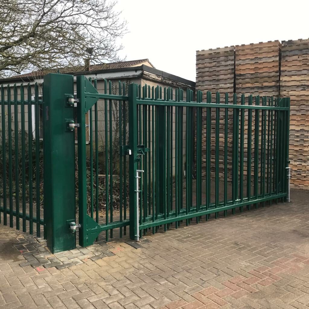 Large green bi-fold gate with palisade fencing using industrial hinges.