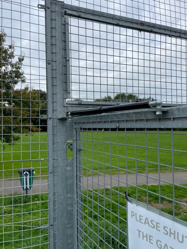 Open gate at tennis club with gate closer installed on top of metal mesh gate