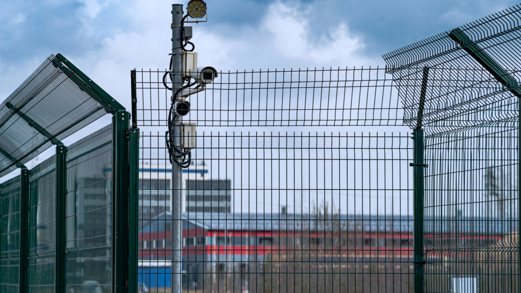 security gate fence with camera behind it and date centre building in the background that is blurred